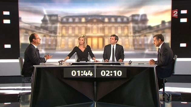 Le 2 mai 2012, 17,8 millions de téléspectateurs suivent le débat entre le président Nicolas Sarkozy (D) et son adversaire socialiste François Hollande, animé par Laurence Ferrari (CG) et David Pujadas (CD) dans un studio de La Plaine Saint-Denis