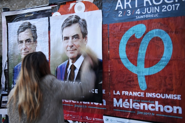 Une militante colle une affiche de F. Fillon sur l'une de la France Insoumise, le 10 avril 2017 à Rennes